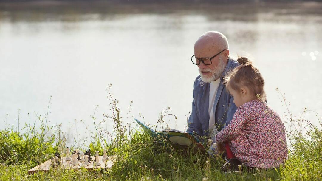 Großvater liest Enkelin an einem See ein Buch vor