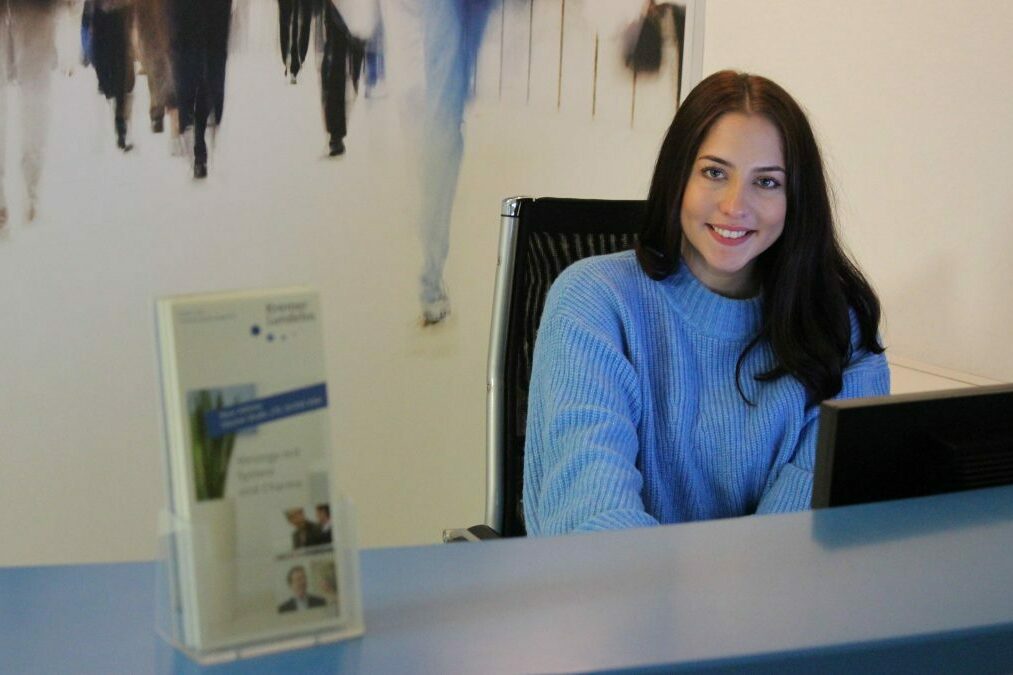 Eine Frau sitzt an einem Schreibtisch und lächelt in die Kamera