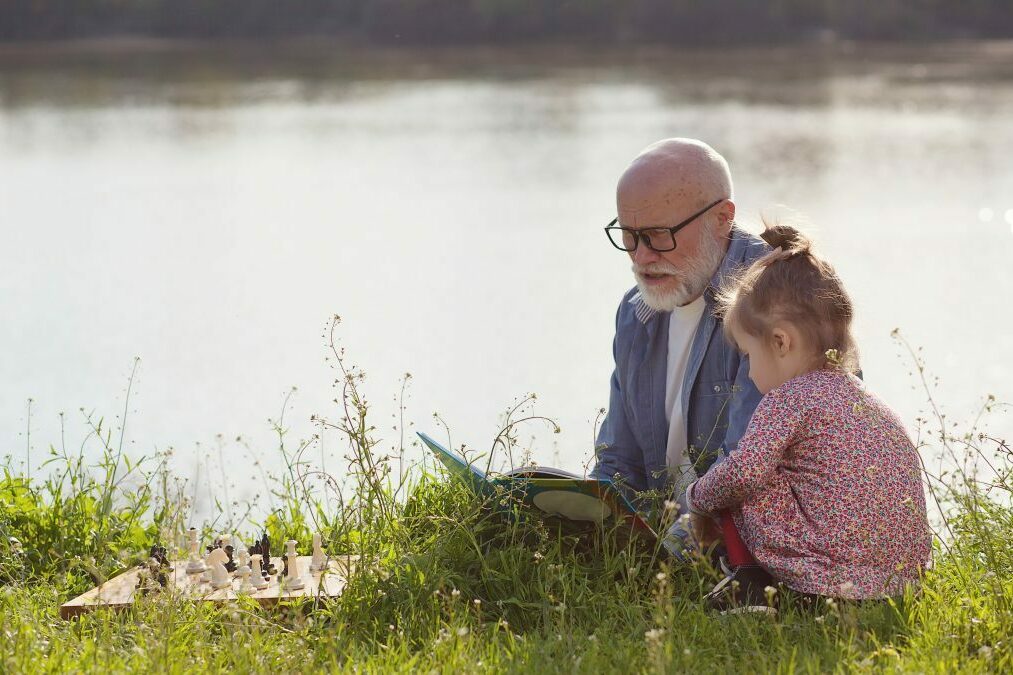Großvater liest Enkelin an einem See ein Buch vor