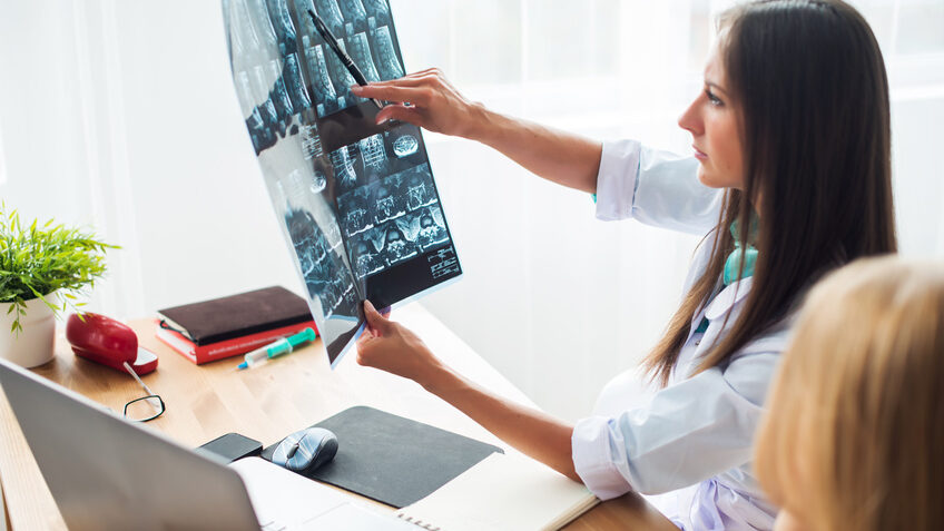 Ärztin sitzt am Schreibtisch und zeigt einer Patienten etwas auf einem Röntgenbild